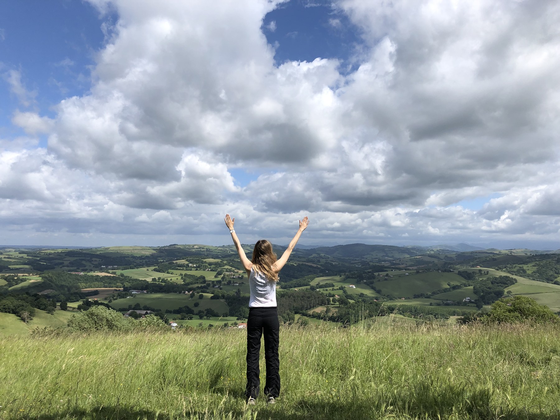 Lisa Kalfus standing on a hilltop with arms raised over the Basque countryside