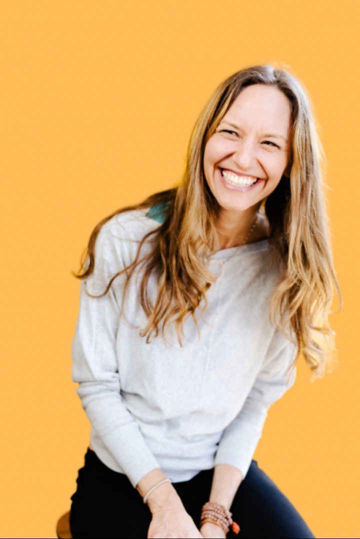 Lisa Kalfus laughing, photographed against a warm orange backdrop