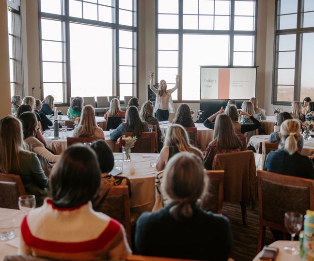 Lisa Kalfus presenting to a room of people seated at round tables