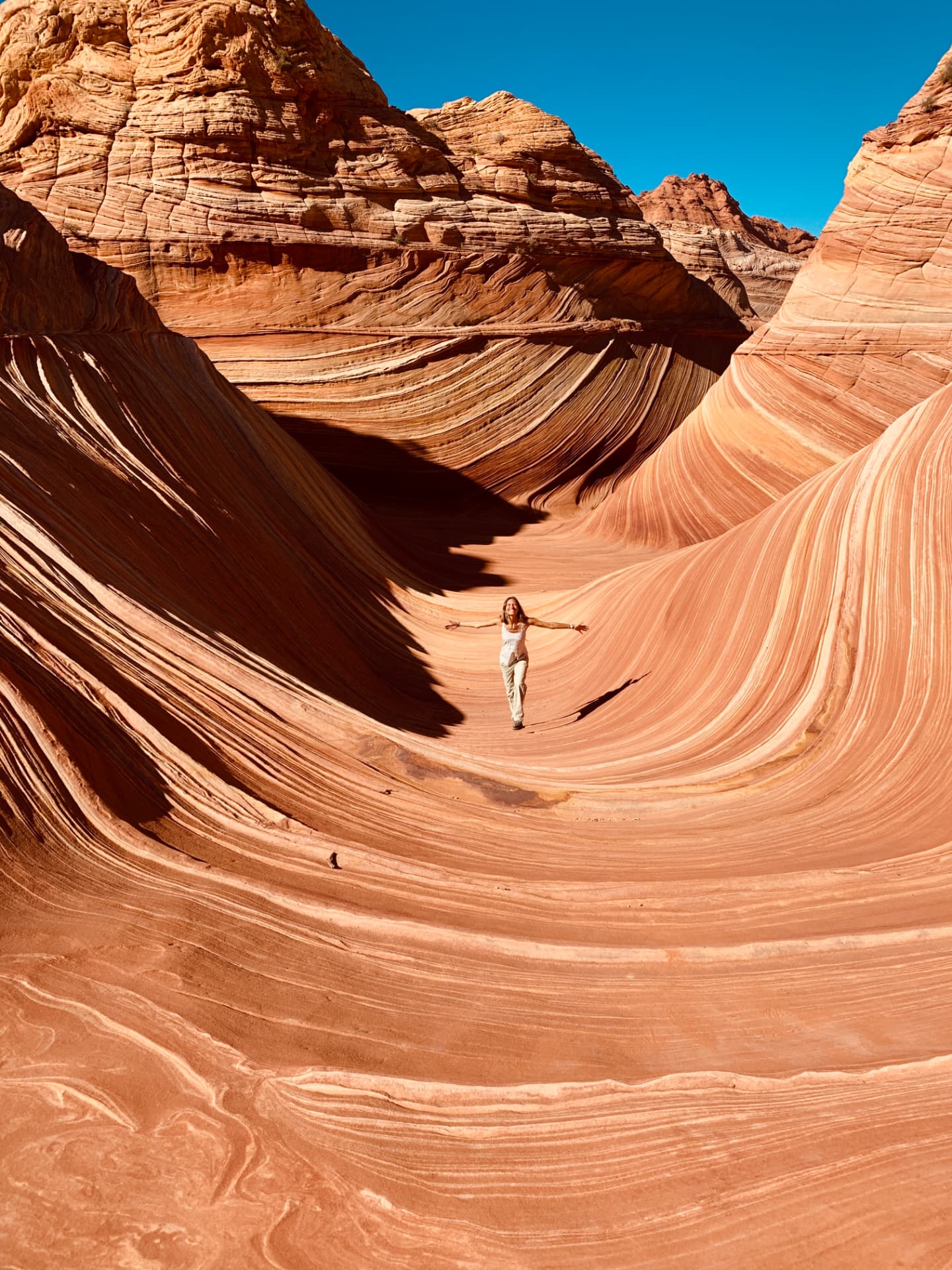 Lisa Kalfus walking with arms outstretched through the sandstone waves of a desert canyon